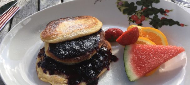 Bialy talerz, na którym znajduje się nalesnik z dżemem a obok kawałki arbuza, pomarańczy i truskawki.