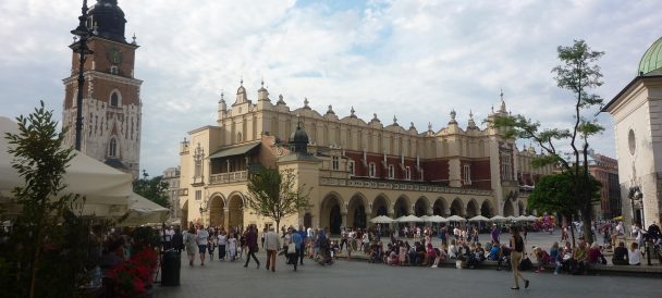 Wieża zwieńczona blaszanym dachem, dekorowana obok z prawej strony bogato zdobiony niski budynek - krakowskie sukiennice