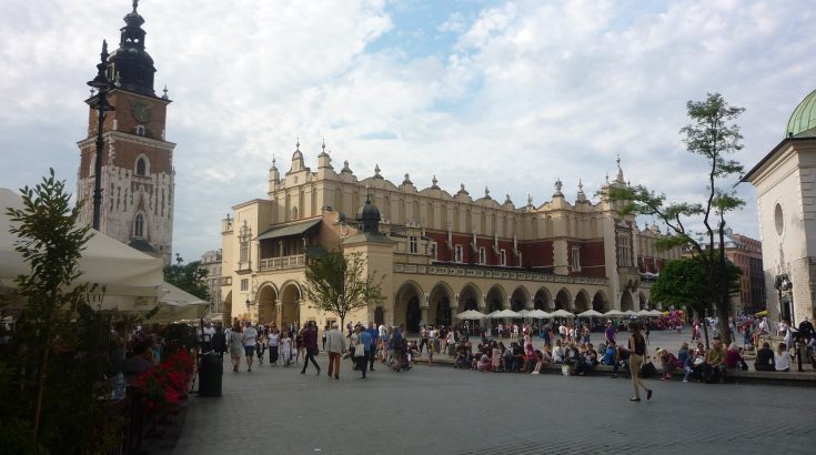 Wieża zwieńczona blaszanym dachem, dekorowana obok z prawej strony bogato zdobiony niski budynek - krakowskie sukiennice