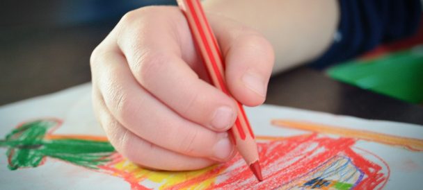 Ręka małego dziecka, które rysuje czerwona kredką rysunek na kartce.