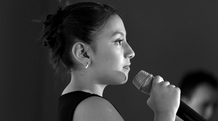 Obrazek przedstawia dziewczynę trzymającą w ręku mikrofon.